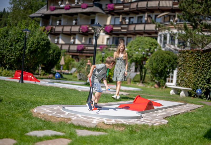 Kinder spielen auf dem hoteleigenen Minigolf-Platz im Familienhotel Ebner's Waldhof am Fuschlsee.