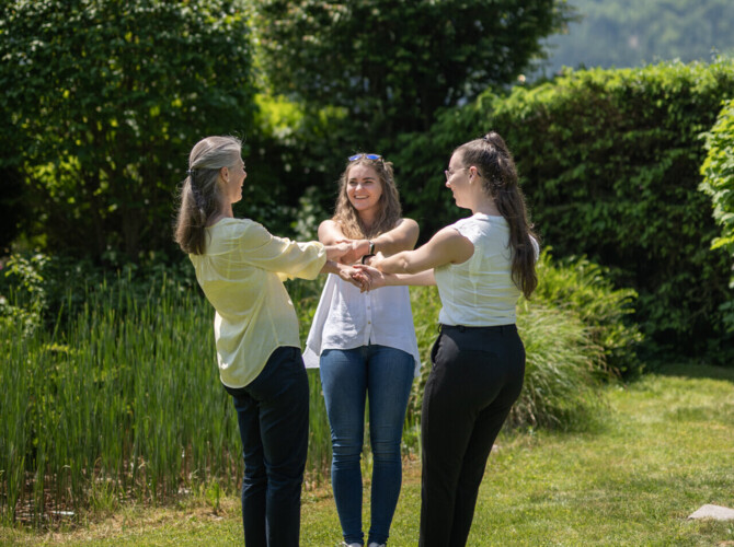 Drei Damen stehen im Kreis und halten sich an den Händen im Garten des Seminarhotel Ebner's Waldhof am Fuschlsee.